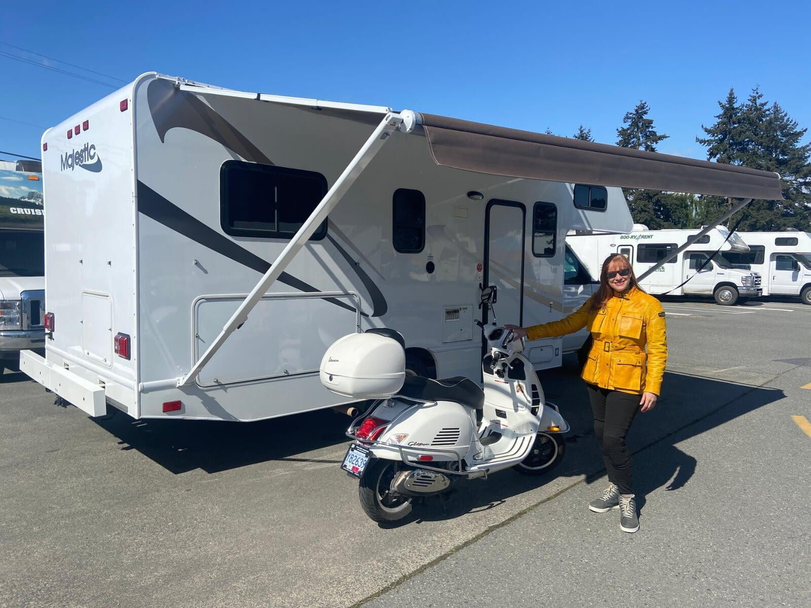 Janice Tylor standing next to a white Vespa, under the awning of her new Majestic 23a Motorhome